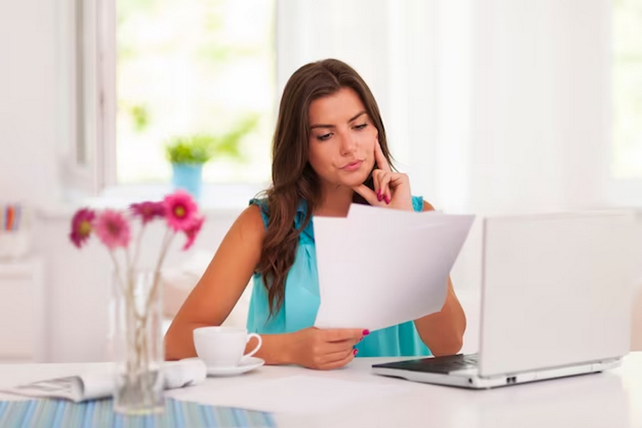 A woman reading documents in front of a laptop.