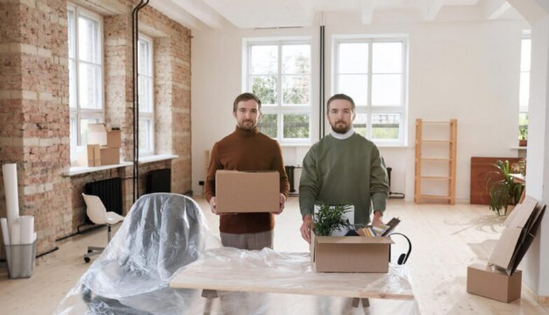 Two individuals holding a box of belongings inside an empty apartment